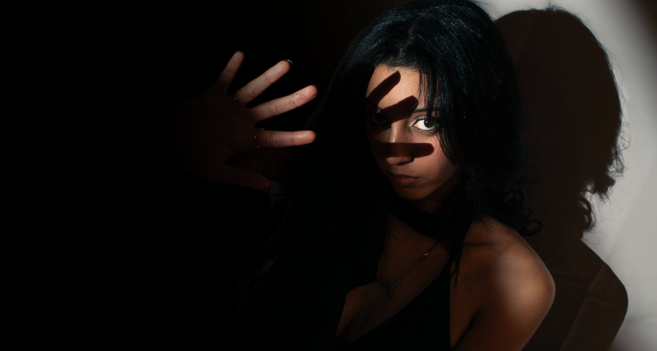 Editorial studio portrait, dramatic side-lit shadow across the face